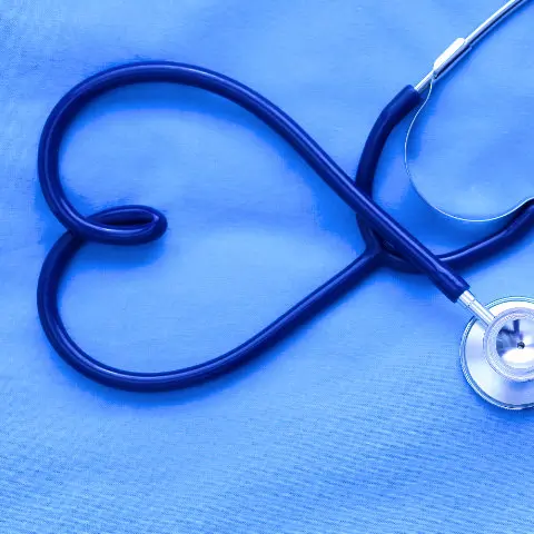 A stethoscope arranged in the shape of a heart on a blue fabric background.