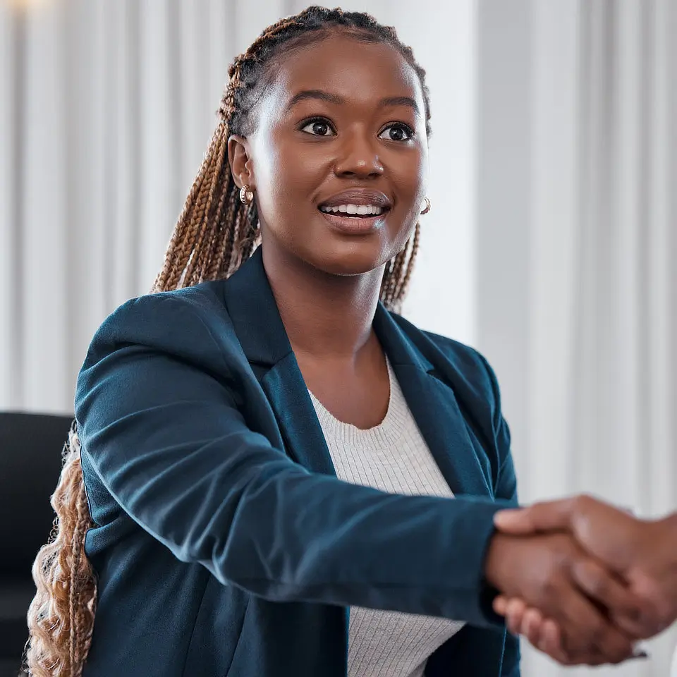 A person with long braided hair and a blue blazer shaking hands with someone outside the frame.