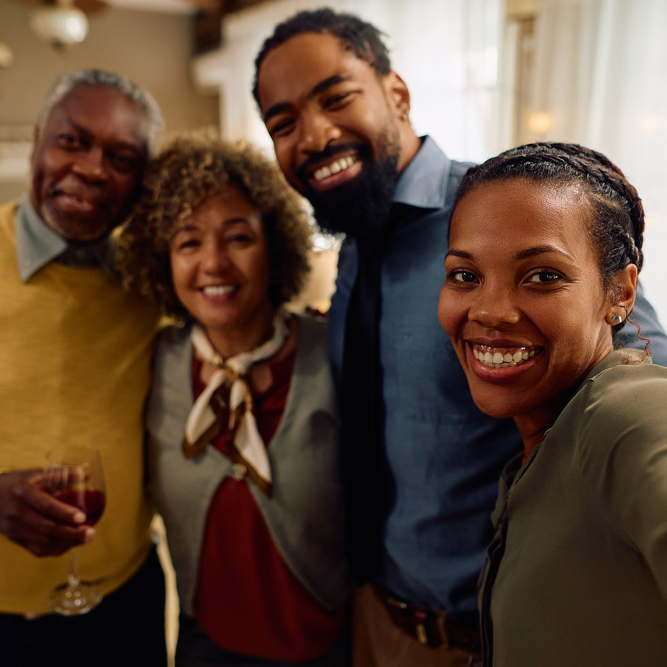 A group of four people smiling indoors, with one person holding a glass of wine.