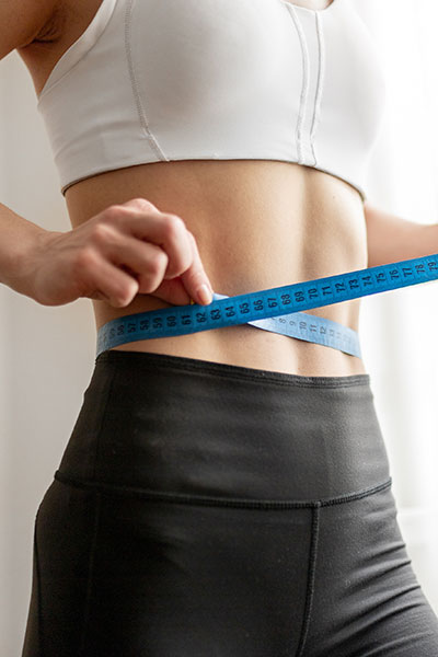 Person in athletic wear measuring their waist with a blue measuring tape.